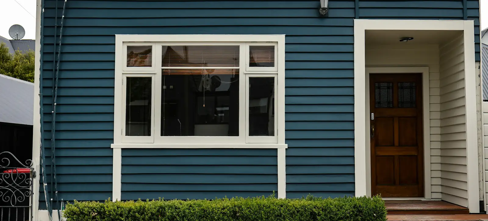 A blue weatherboard villa with a white-framed front door