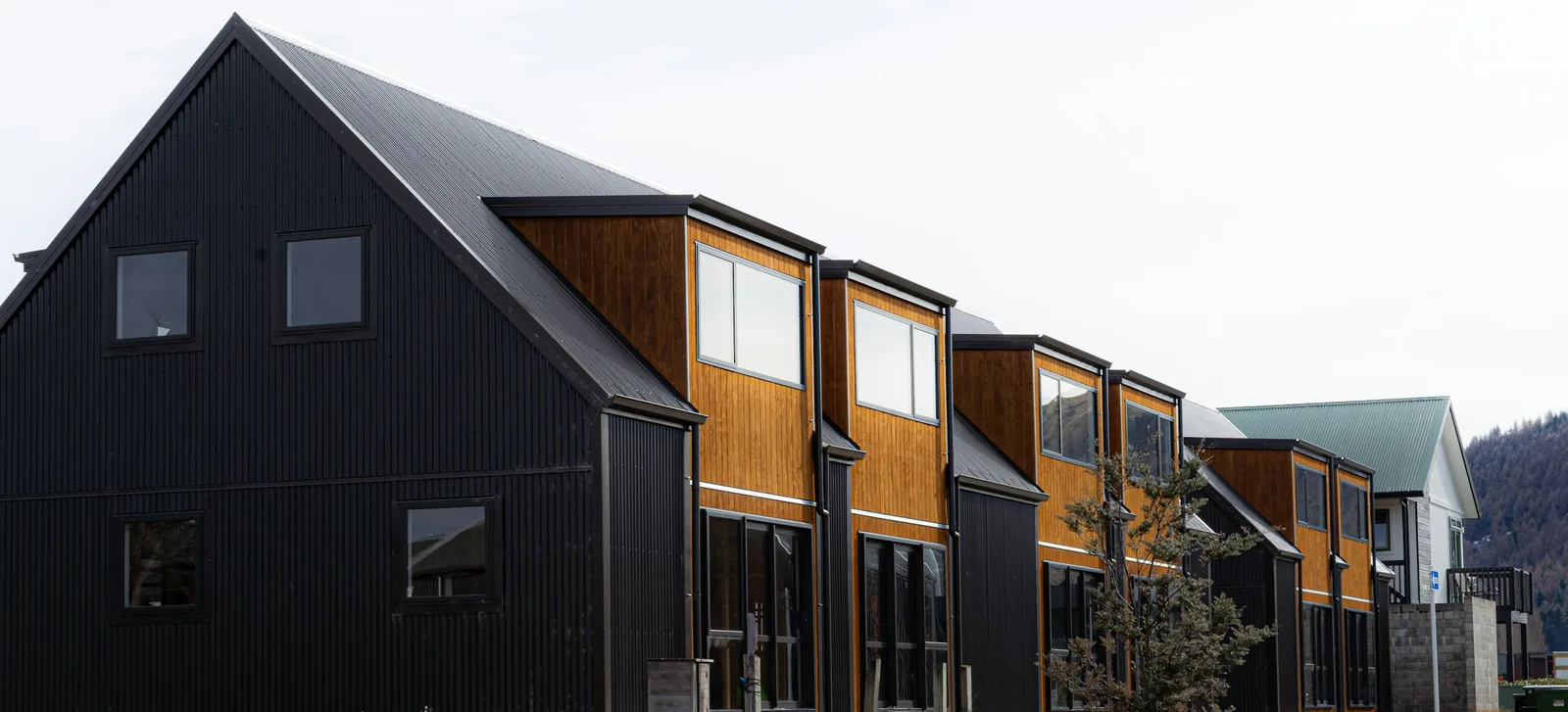 A row of new black and timber townhouses below the hills